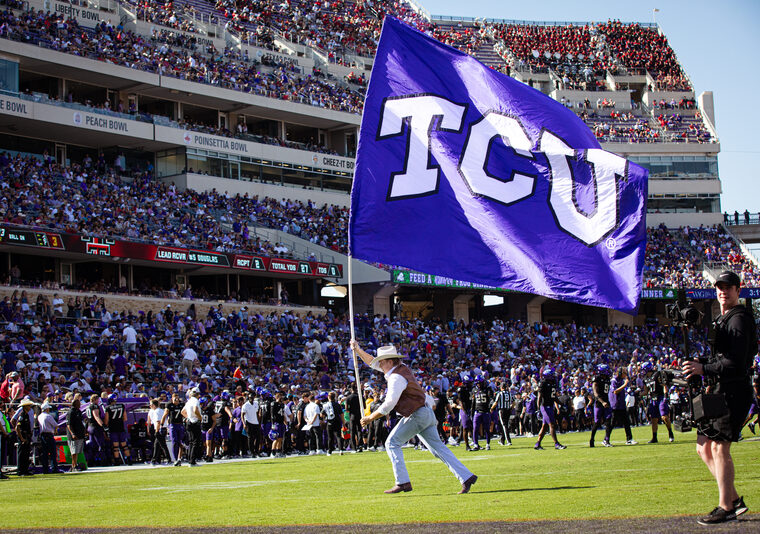 A TCU Ranger runs across the football field waving a giant TCU flag